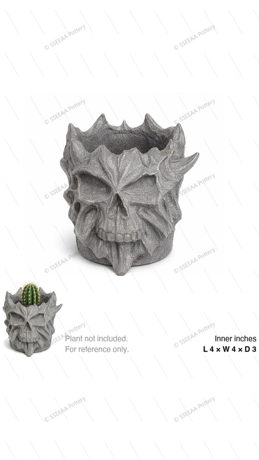 Gray skull-faced decorative pot with a sculptural rocky surface and raised rim details, shown with a small cactus for scale.