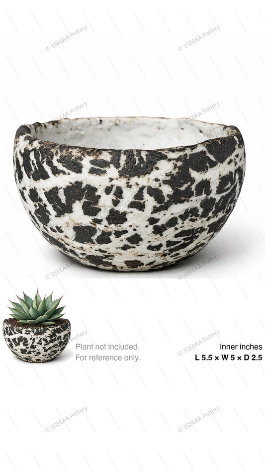 A shallow bone-white speckled pot with bold black patchwork finish and rounded rim.